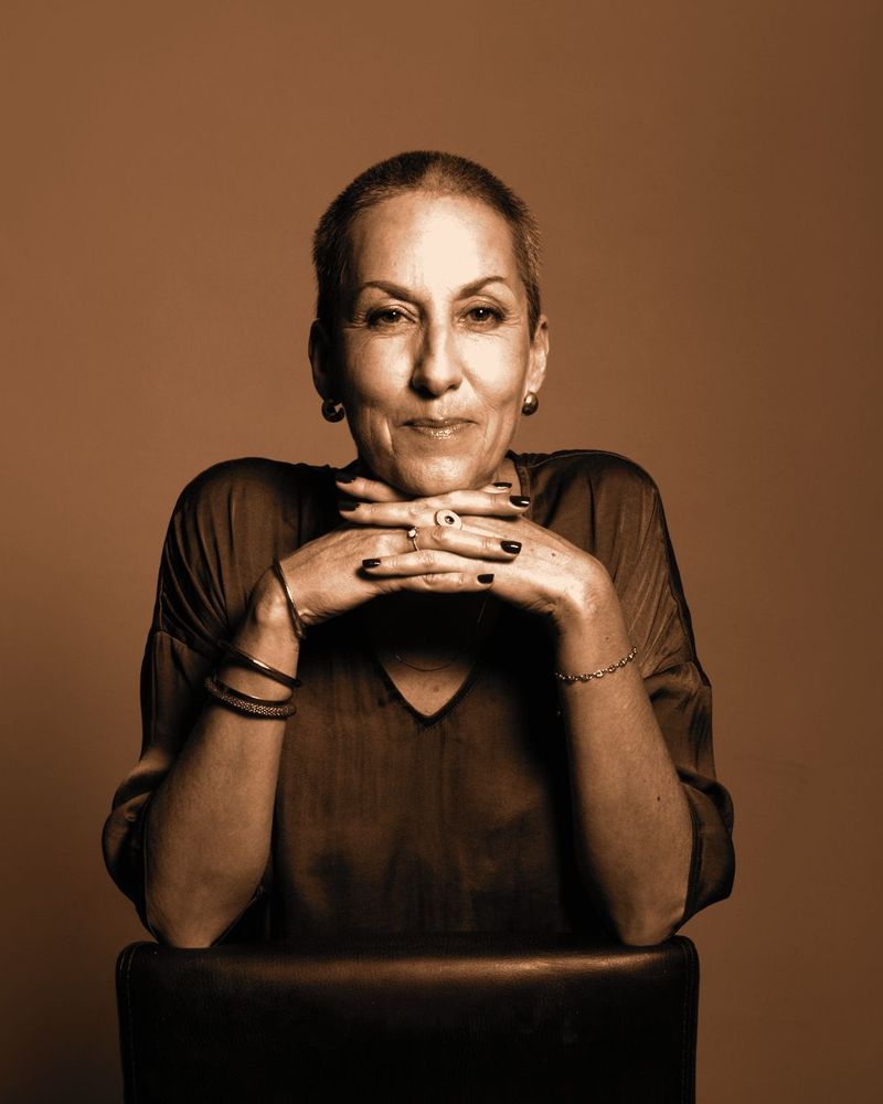 Portrait de Nathalie Merle, cheveux courts, mains croisées sous le menton, en studio.