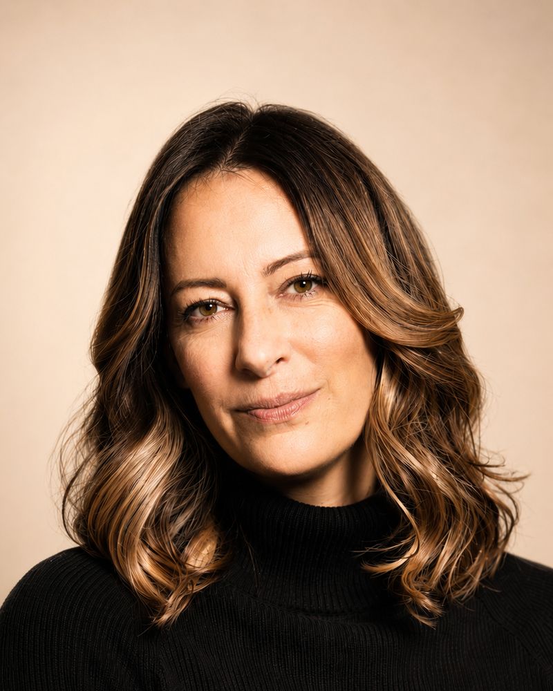 Portrait de Sophie Artonne, cheveux longs, pull noir, sur fond beige.